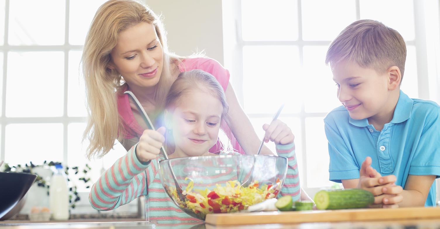 Family looking at girl mixing salad in kitchen