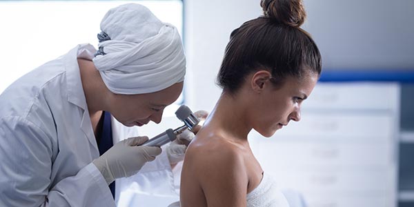 Side view of a mature mixed race female doctor checking the body of a Caucasian female patient with dermatoscopy in a clinic